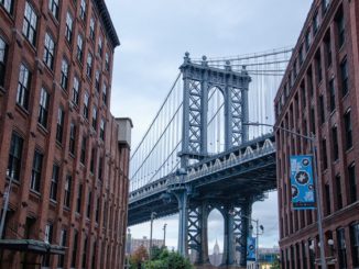 The Brooklyn Bridge between two rows of buildings in DUMBO, New York