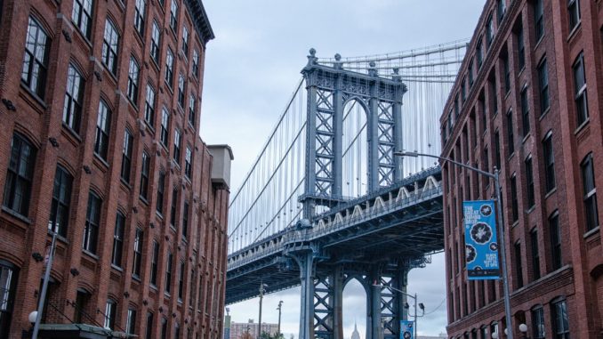 The Brooklyn Bridge between two rows of buildings in DUMBO, New York