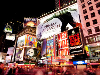 Night scene of Broadway at Times Square in Manhattan (New York City) with all the lit up billboards and advertisements, and many tourists people walking by.
