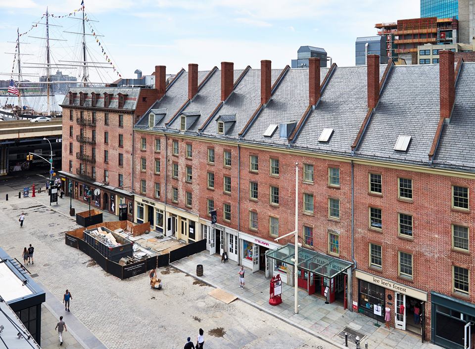South Street Seaport Museum with ship in background and padestrians walking past shops undernearth
