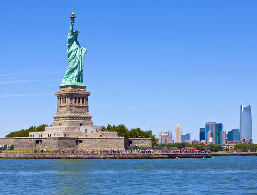 Tourists gather underneath the Statue of Liberty on a clear day