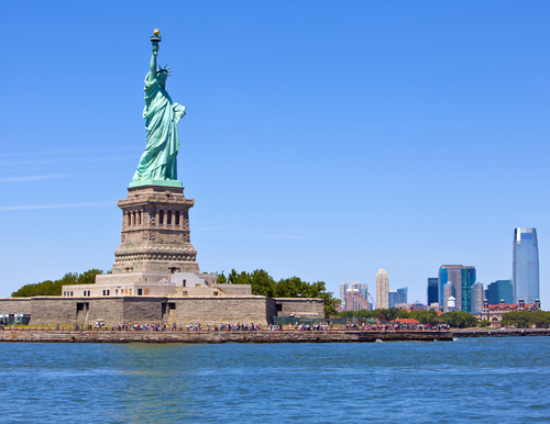 Tourists gather underneath the Statue of Liberty on a clear day