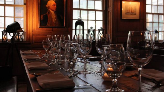 Empty glasses sit on wooden table in front of a portrait, at New York City’s Fraunces Tavern