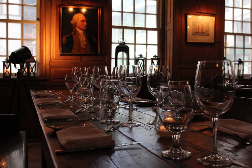 Empty glasses sit on wooden table in front of a portrait, at New York City’s Fraunces Tavern