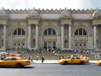 Yellow taxis fly past people queuing outside the Metropolitan Museum of Art located on Fifth Avenue, New York