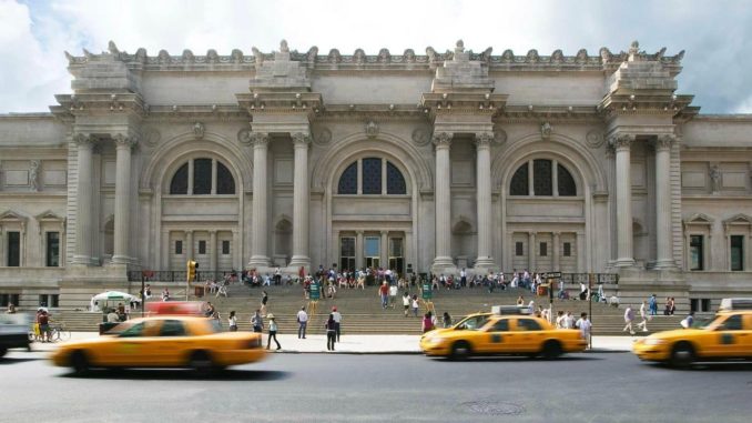 Yellow taxis fly past people queuing outside the Metropolitan Museum of Art located on Fifth Avenue, New York