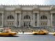 Yellow taxis fly past people queuing outside the Metropolitan Museum of Art located on Fifth Avenue, New York