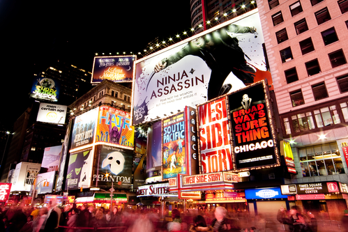 Night scene of Broadway at Times Square in Manhattan (New York City) with all the lit up billboards and advertisements, and many tourists people walking by.