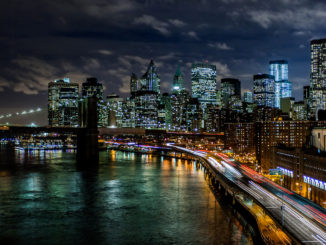 New York at night time, with cars driving past illuminated skyscrapers