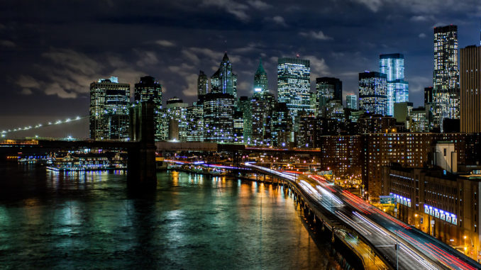 New York at night time, with cars driving past illuminated skyscrapers