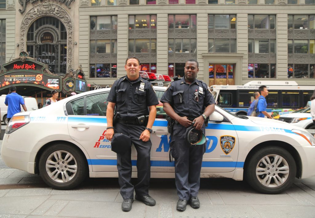 2 police officers stand in front of their vehicle in times square