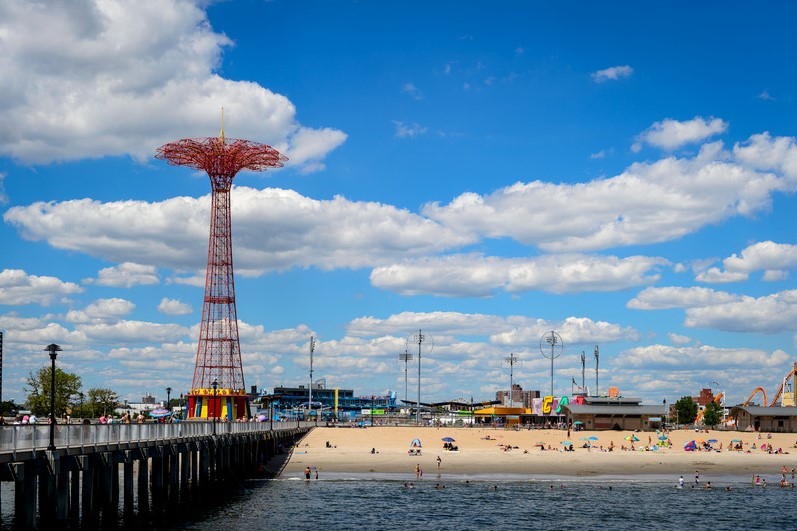 People sunbathe on Coney Island beach in front of fairground